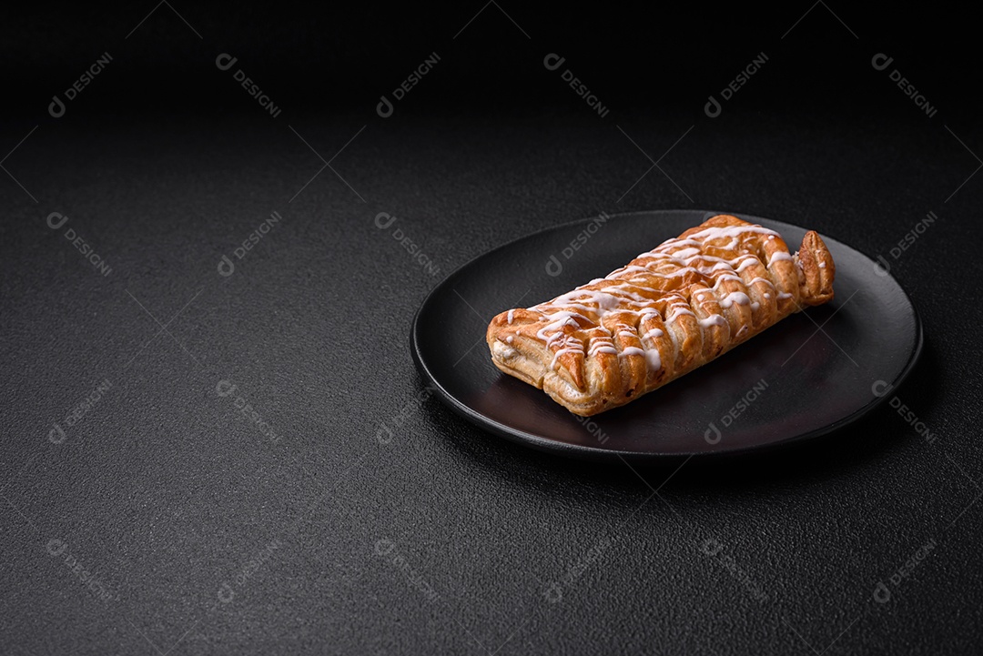 Delicioso pão trançado crocante com passas dentro e glacê branco fora sobre um fundo escuro de concreto