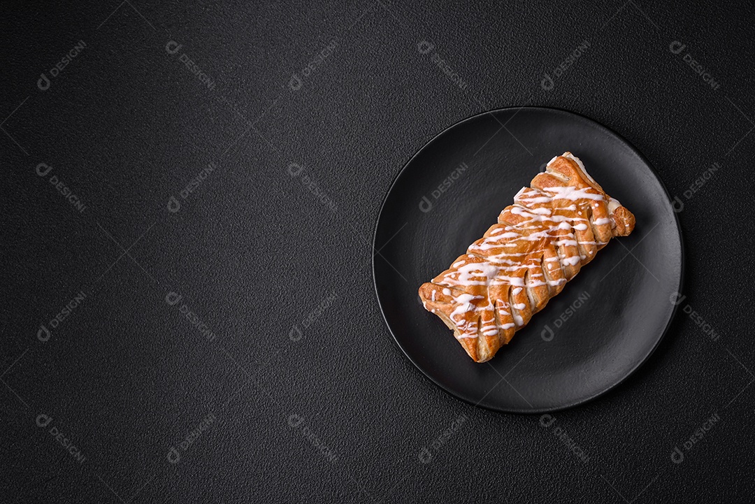Delicioso pão trançado crocante com passas dentro e glacê branco fora sobre um fundo escuro de concreto