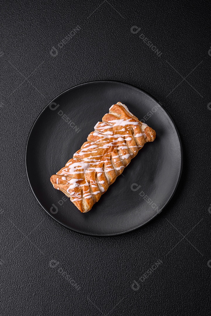 Delicioso pão trançado crocante com passas dentro e glacê branco fora sobre um fundo escuro de concreto