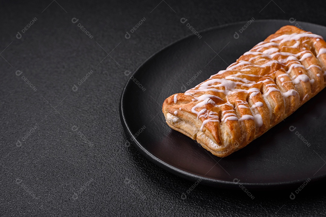 Delicioso pão trançado crocante com passas dentro e glacê branco fora sobre um fundo escuro de concreto