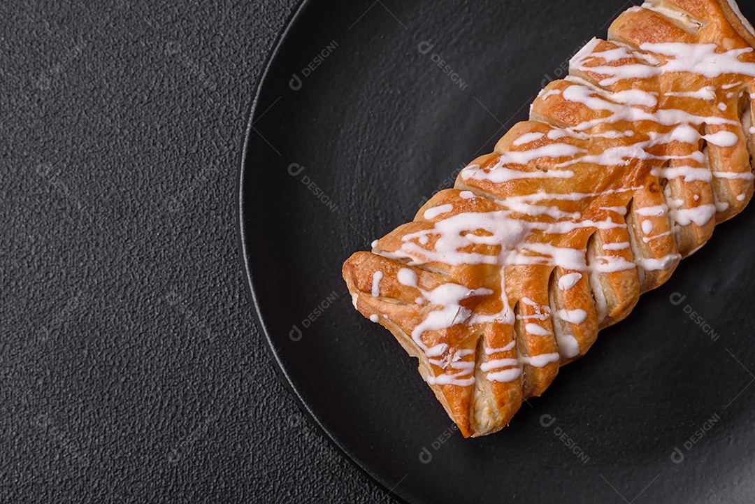 Delicioso pão trançado crocante com passas dentro e glacê branco fora sobre um fundo escuro de concreto