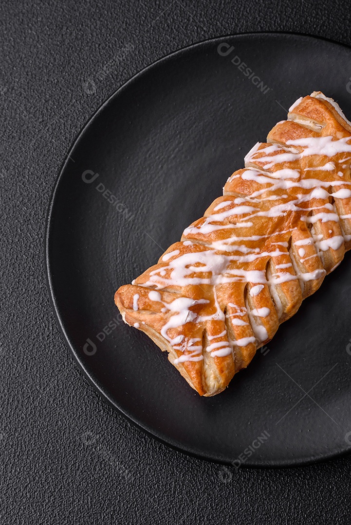 Delicioso pão trançado crocante com passas dentro e glacê branco fora sobre um fundo escuro de concreto
