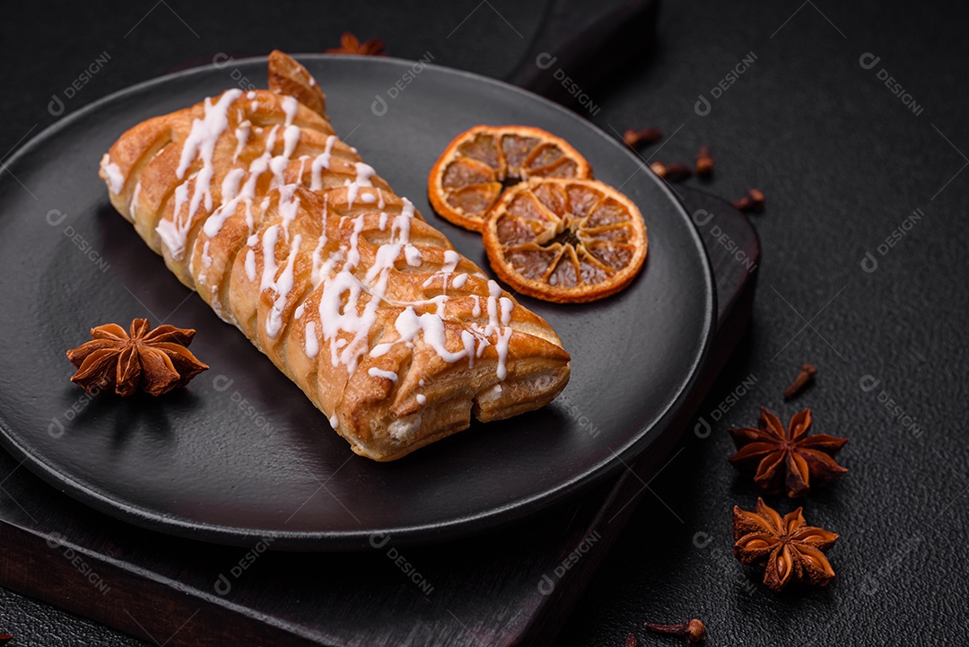 Delicioso pão trançado crocante com passas dentro e glacê branco fora sobre um fundo escuro de concreto