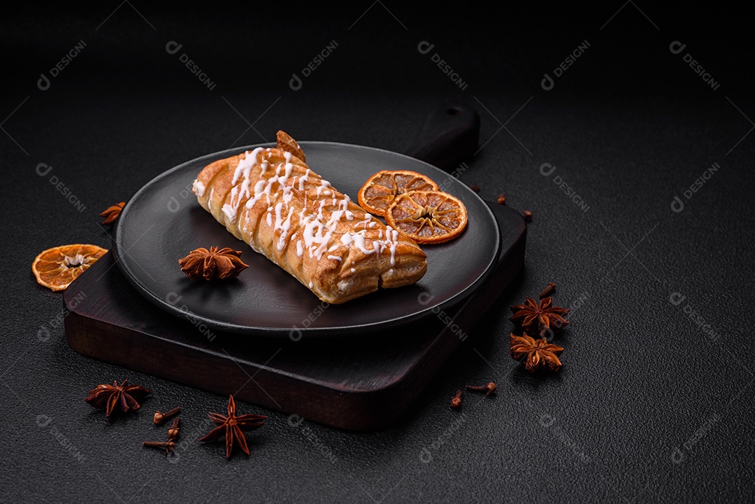 Delicioso pão trançado crocante com passas dentro e glacê branco fora sobre um fundo escuro de concreto