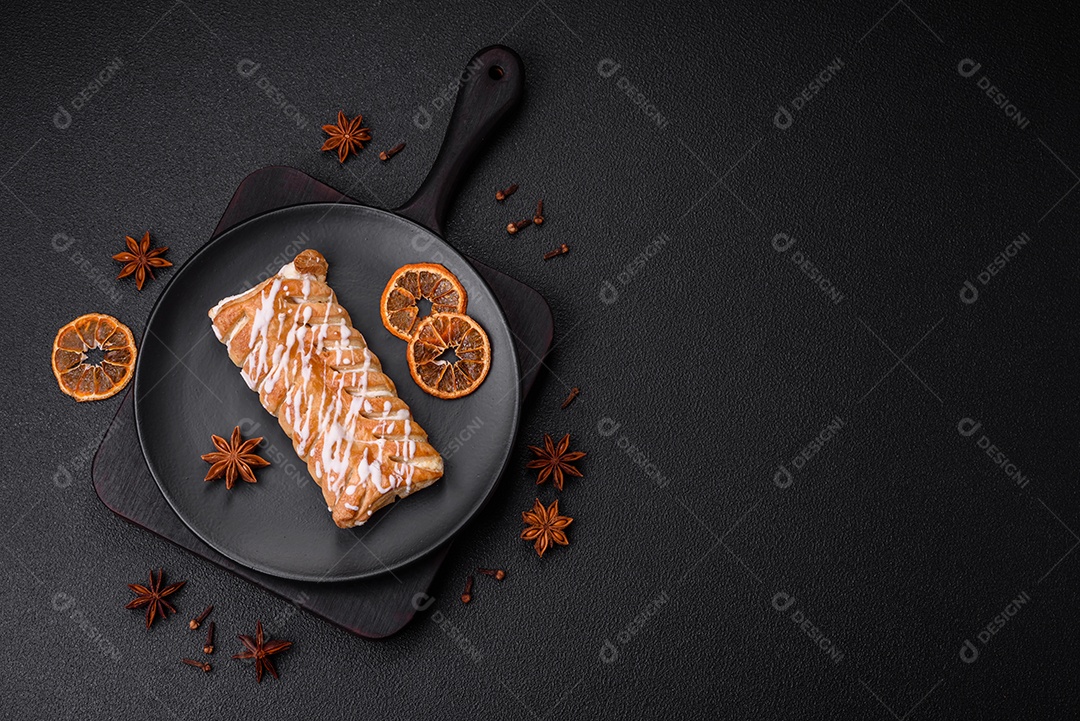 Delicioso pão trançado crocante com passas dentro e glacê branco fora sobre um fundo escuro de concreto