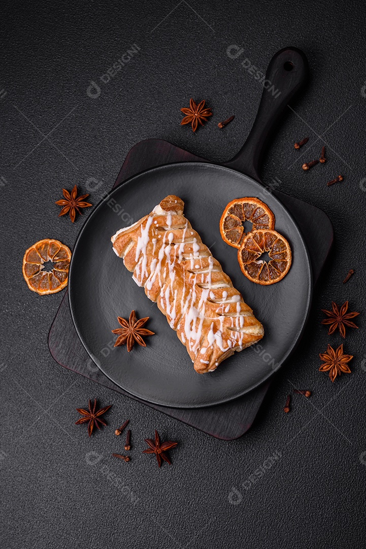 Delicioso pão trançado crocante com passas dentro e glacê branco fora sobre um fundo escuro de concreto