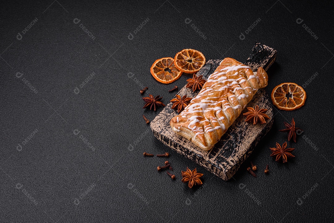 Delicioso pão trançado crocante com passas dentro e glacê branco fora sobre um fundo escuro de concreto