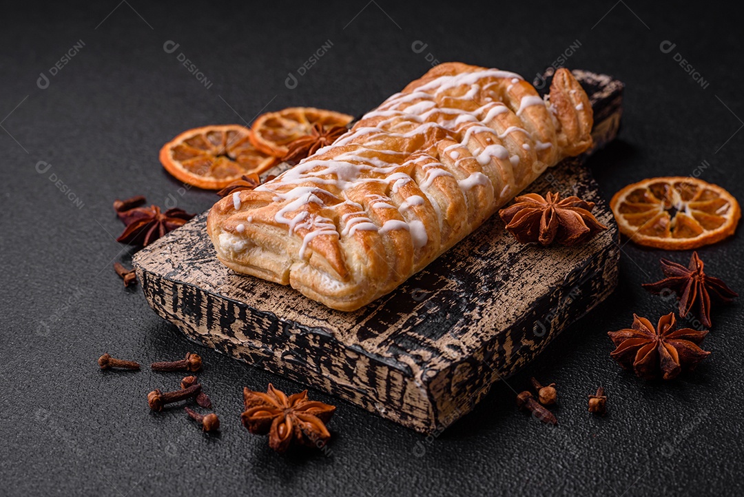 Delicioso pão trançado crocante com passas dentro e glacê branco fora sobre um fundo escuro de concreto
