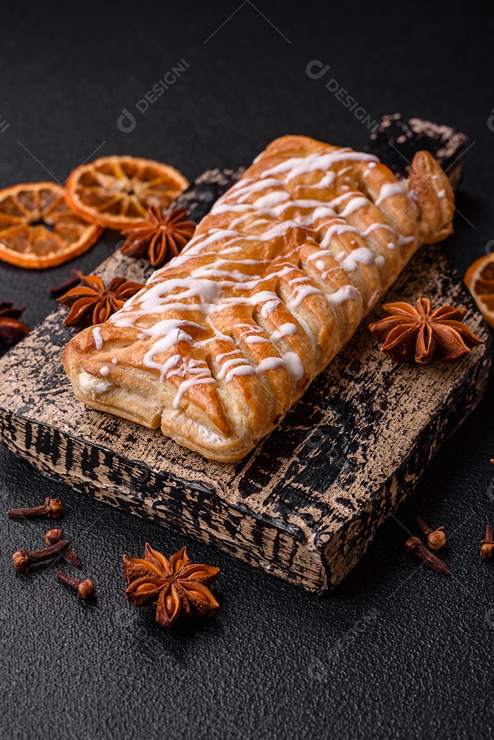 Delicioso pão trançado crocante com passas dentro e glacê branco fora sobre um fundo escuro de concreto