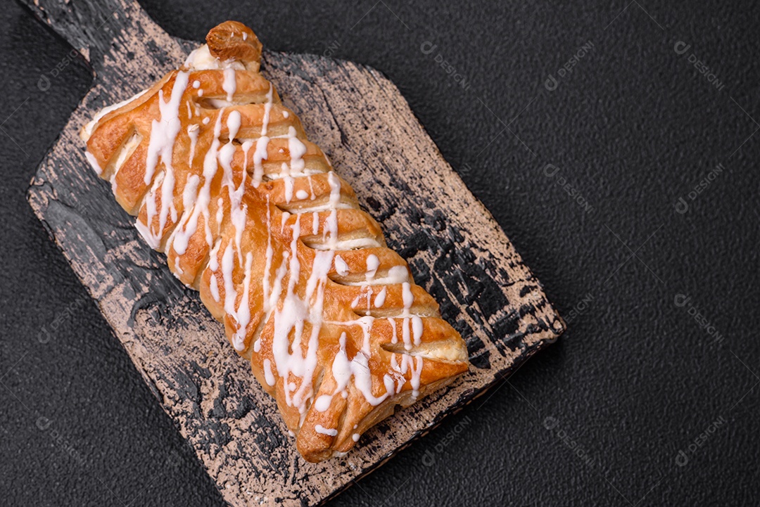 Delicioso pão trançado crocante com passas dentro e glacê branco fora sobre um fundo escuro de concreto