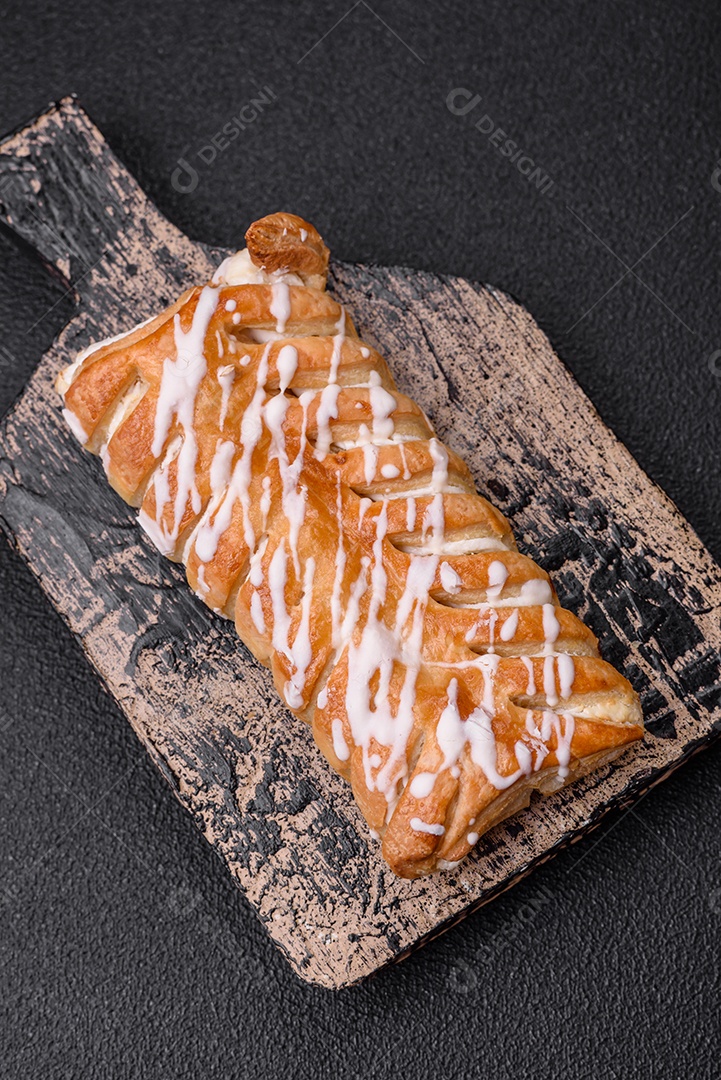 Delicioso pão trançado crocante com passas dentro e glacê branco fora sobre um fundo escuro de concreto