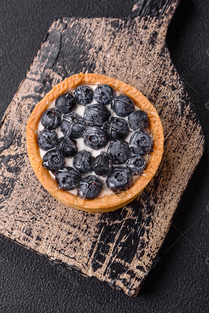 Deliciosa torta redonda doce e fresca com mirtilos maduros e creme sobre um fundo escuro de concreto