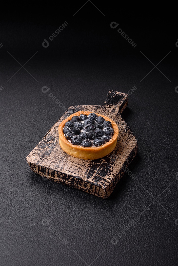 Deliciosa torta redonda doce e fresca com mirtilos maduros e creme sobre um fundo escuro de concreto