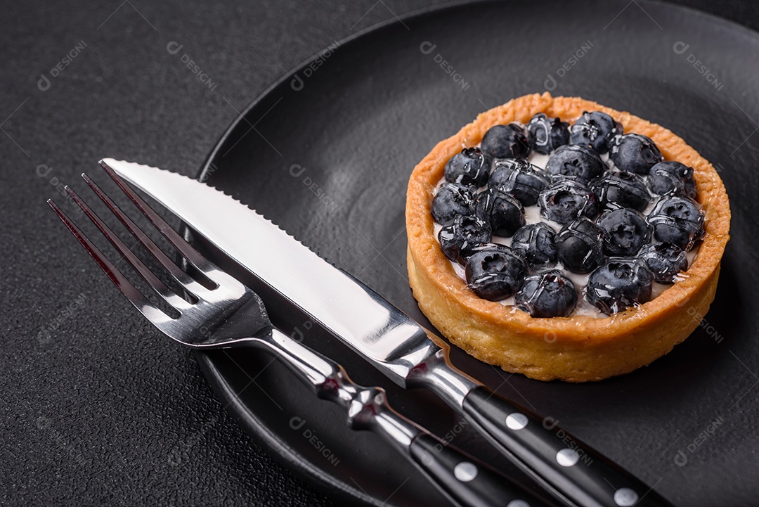 Deliciosa torta redonda doce e fresca com mirtilos maduros e creme sobre um fundo escuro de concreto