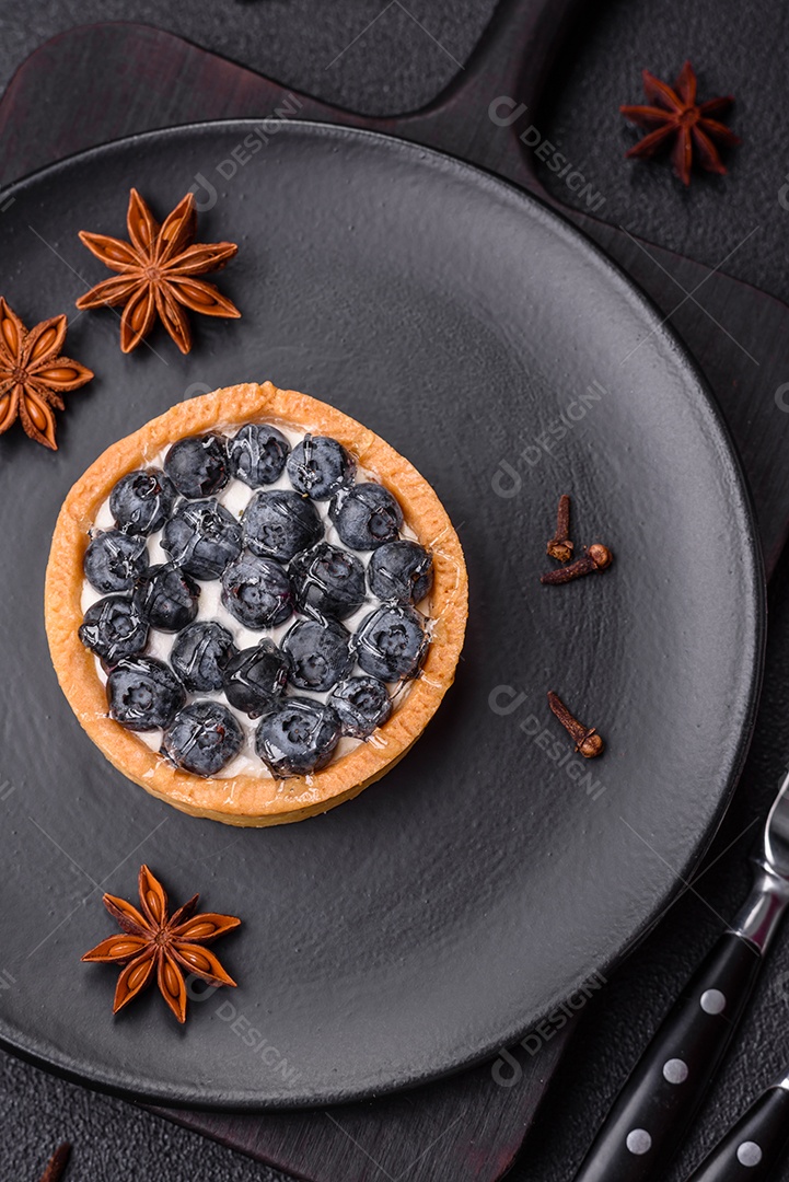 Deliciosa torta redonda doce e fresca com mirtilos maduros e creme sobre um fundo escuro de concreto