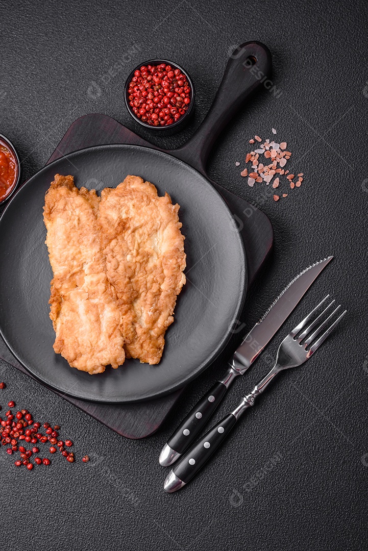 Deliciosa costeleta de frango frito ou carne de porco frita à milanesa com sal, especiarias e ervas sobre um fundo escuro de concreto