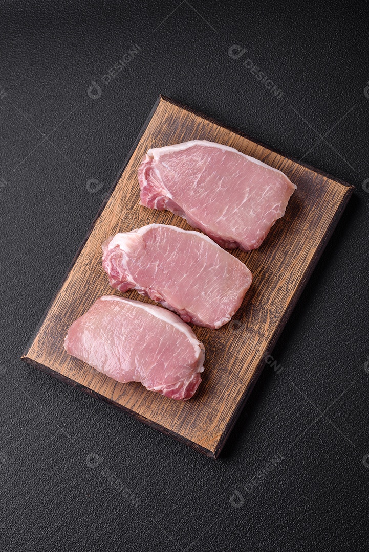 Bife de carne de porco fresca crua com sal, especiarias e ervas numa tábua de madeira