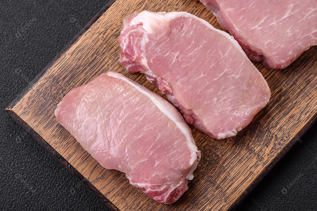 Bife de carne de porco fresca crua com sal, especiarias e ervas numa tábua de madeira