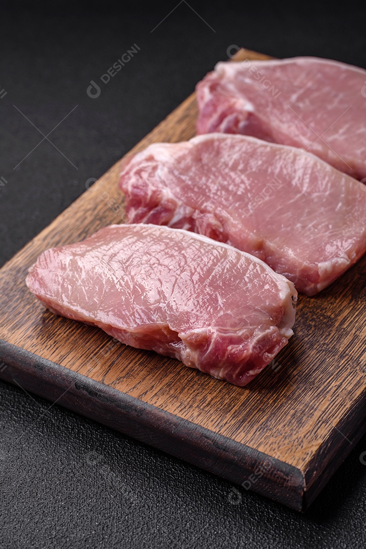 Bife de carne de porco fresca crua com sal, especiarias e ervas numa tábua de madeira