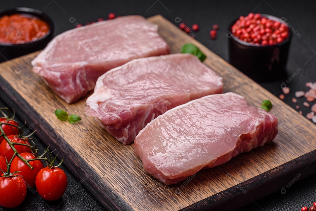 Bife de carne de porco fresca crua com sal, especiarias e ervas numa tábua de madeira