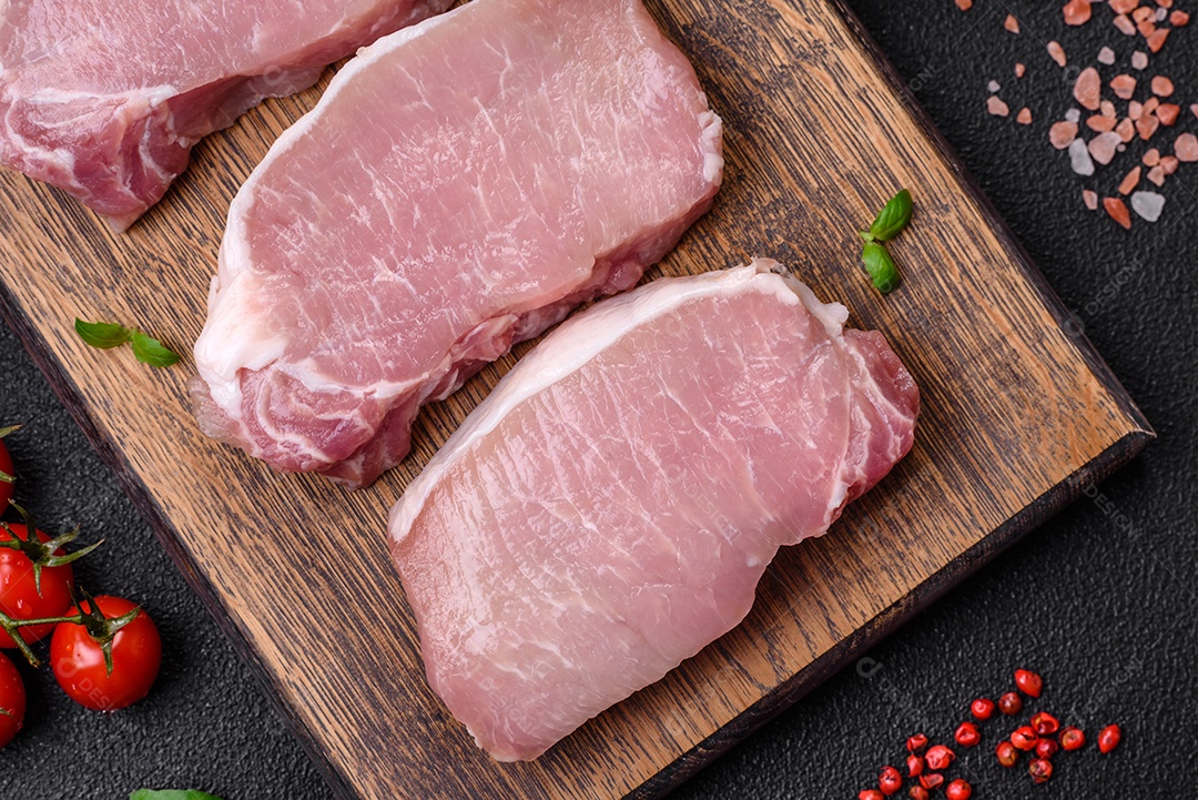 Bife de carne de porco fresca crua com sal, especiarias e ervas numa tábua de madeira