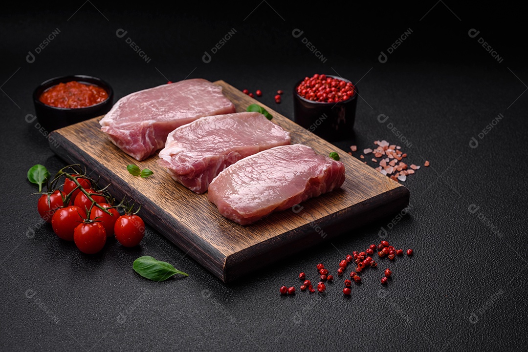 Bife de carne de porco fresca crua com sal, especiarias e ervas numa tábua de madeira