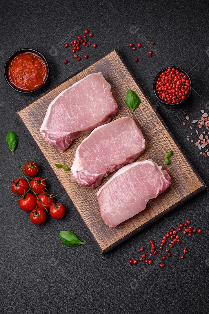 Bife de carne de porco fresca crua com sal, especiarias e ervas numa tábua de madeira