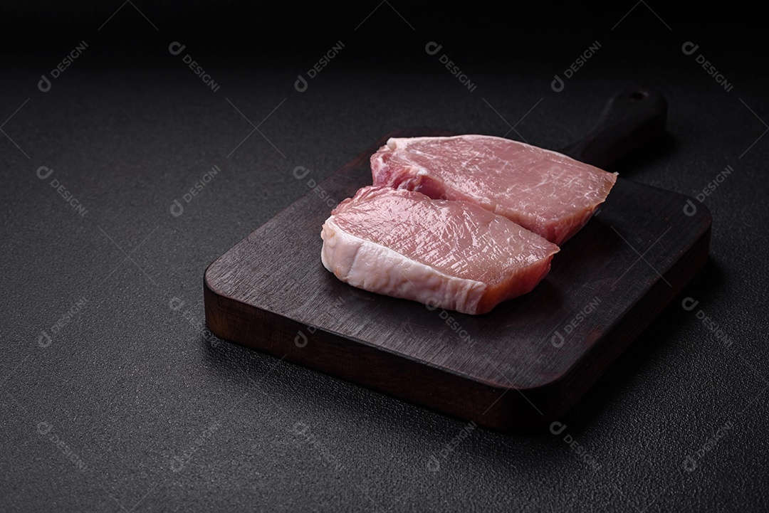 Bife de filé mignon cru com sal, especiarias e ervas em um fundo escuro de concreto