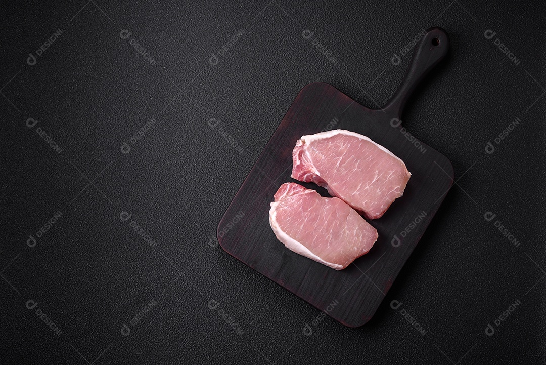 Bife de carne de porco fresca crua com sal, especiarias e ervas numa tábua de madeira