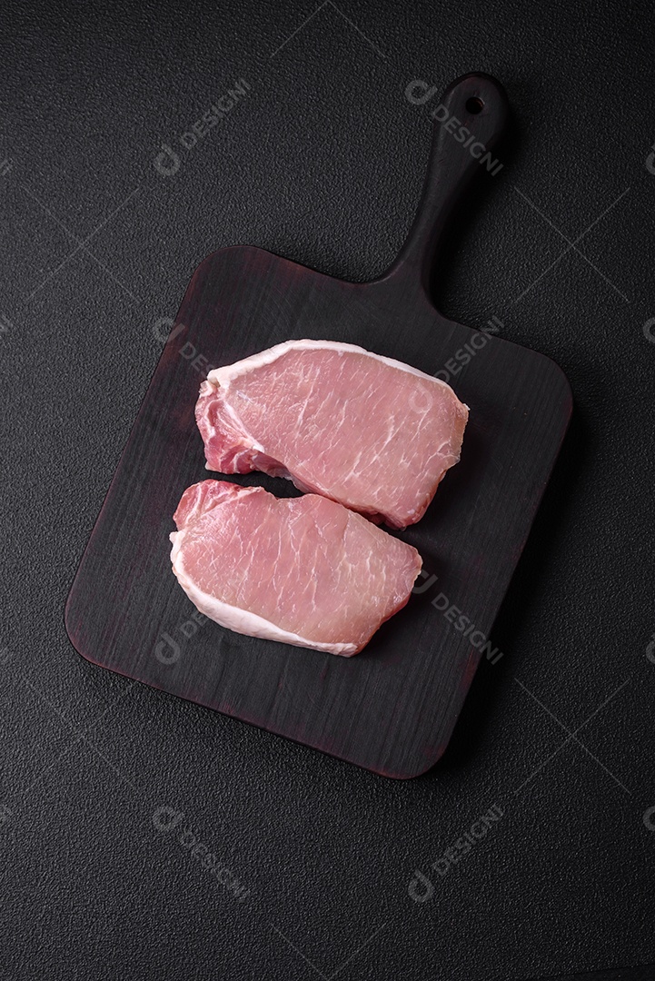 Bife de carne de porco fresca crua com sal, especiarias e ervas numa tábua de madeira