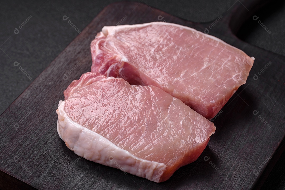 Bife de carne de porco fresca crua com sal, especiarias e ervas numa tábua de madeira