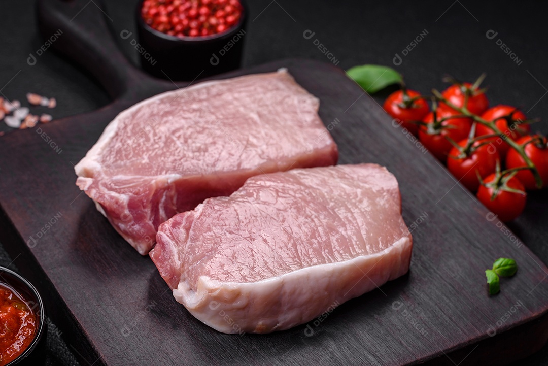 Bife de carne de porco fresca crua com sal, especiarias e ervas numa tábua de madeira