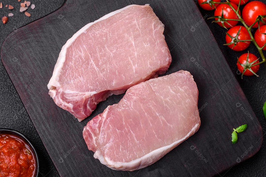 Bife de carne de porco fresca crua com sal, especiarias e ervas numa tábua de madeira