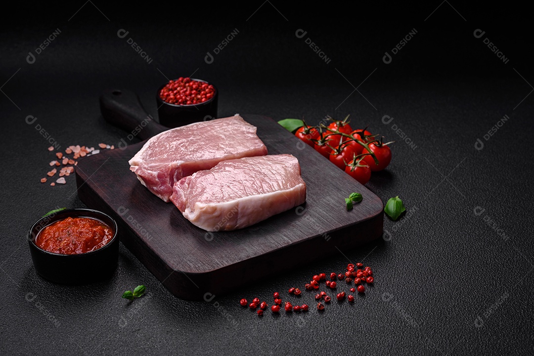 Bife de carne de porco fresca crua com sal, especiarias e ervas numa tábua de madeira