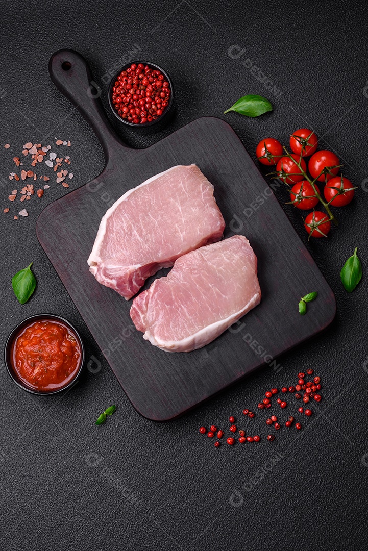 Bife de carne de porco fresca crua com sal, especiarias e ervas numa tábua de madeira