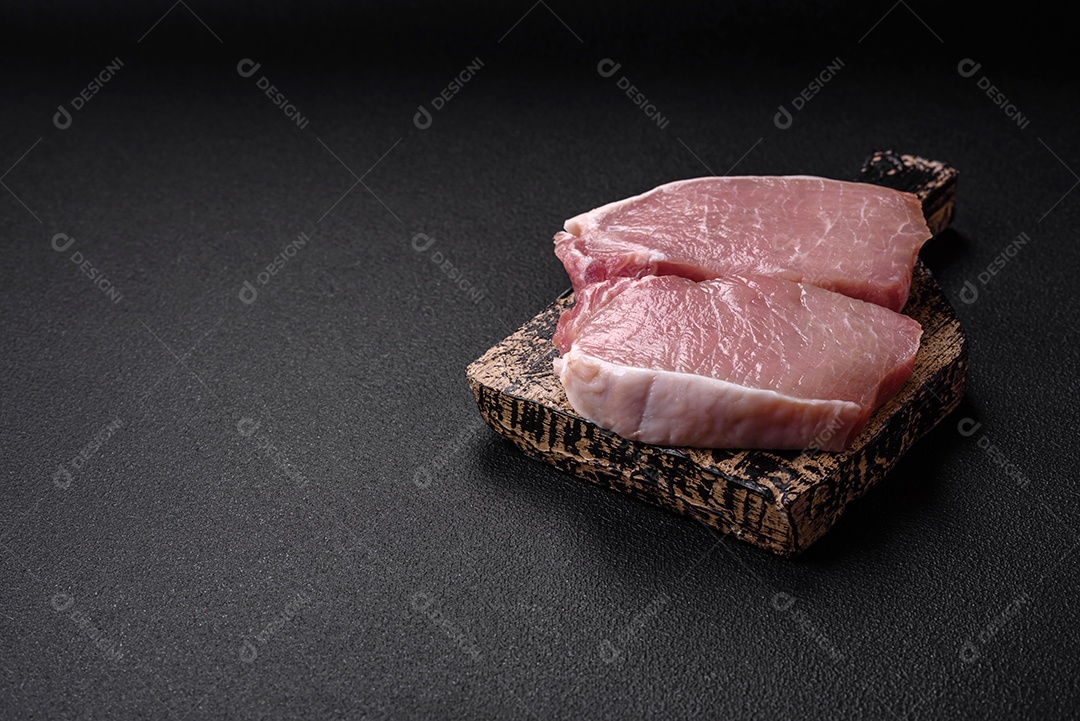 Bife de carne de porco fresca crua com sal, especiarias e ervas numa tábua de madeira