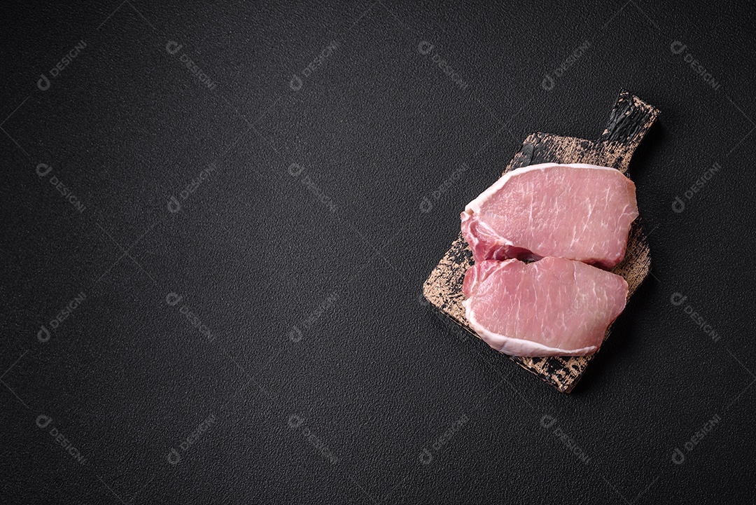 Bife de filé mignon cru com sal, especiarias e ervas em um fundo escuro de concreto