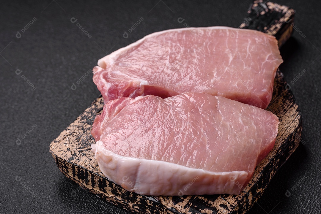 Bife de carne de porco fresca crua com sal, especiarias e ervas numa tábua de madeira