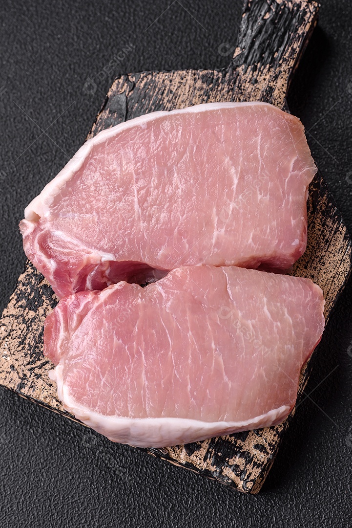 Bife de carne de porco fresca crua com sal, especiarias e ervas numa tábua de madeira