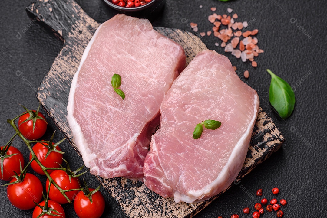 Bife de carne de porco fresca crua com sal, especiarias e ervas numa tábua de madeira