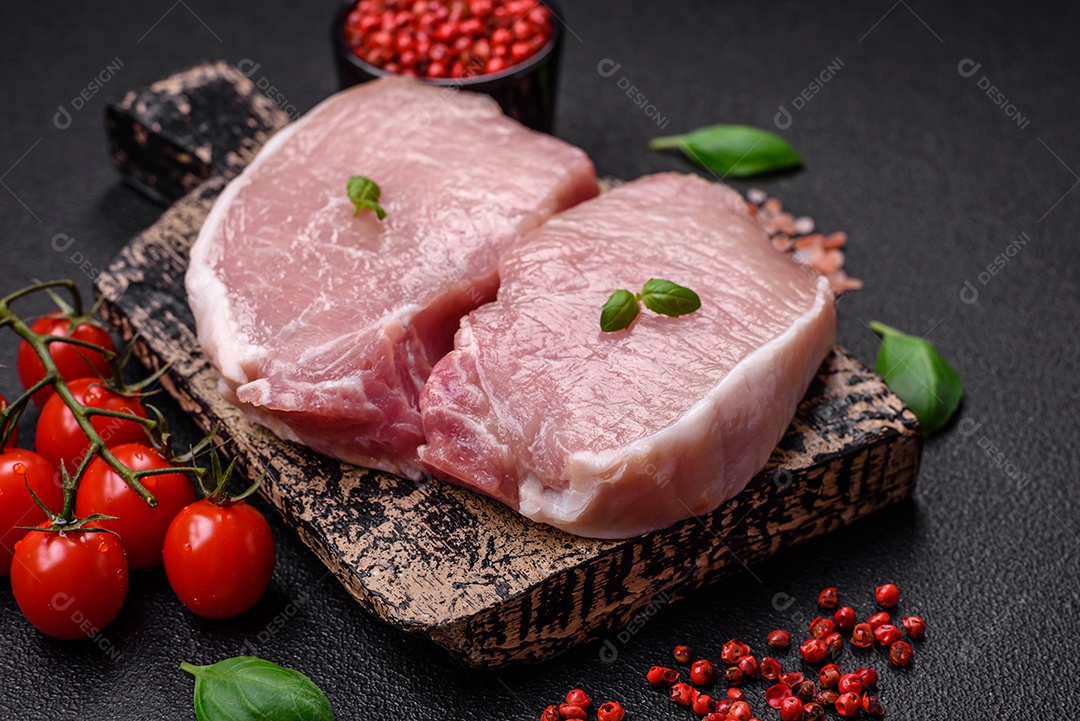 Bife de carne de porco fresca crua com sal, especiarias e ervas numa tábua de madeira