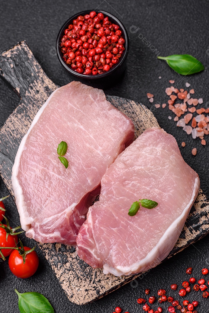 Bife de carne de porco fresca crua com sal, especiarias e ervas numa tábua de madeira