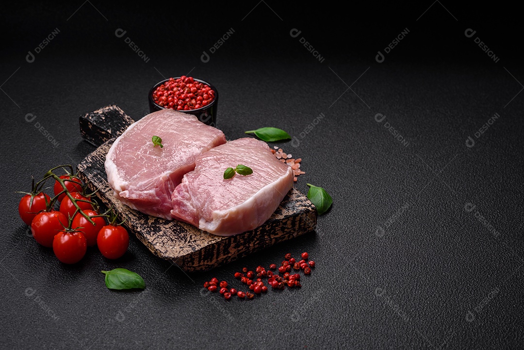 Bife de filé mignon cru com sal, especiarias e ervas em um fundo escuro de concreto