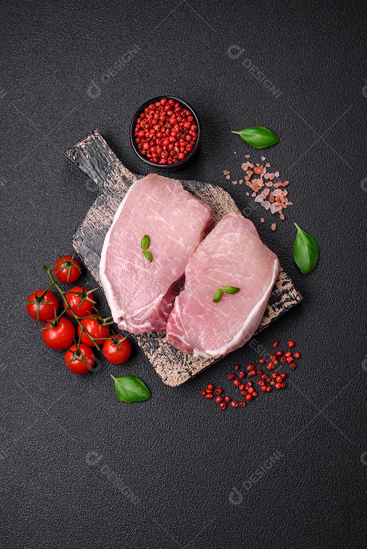 Bife de carne de porco fresca crua com sal, especiarias e ervas numa tábua de madeira