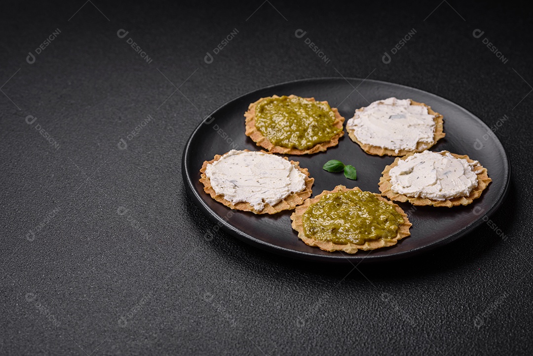 Petiscos redondos com chips crocantes ou biscoitos com cream cheese e pesto num prato de cerâmica