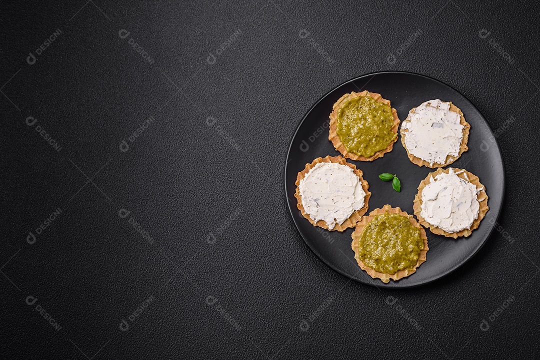Petiscos redondos com chips crocantes ou biscoitos com cream cheese e pesto num prato de cerâmica