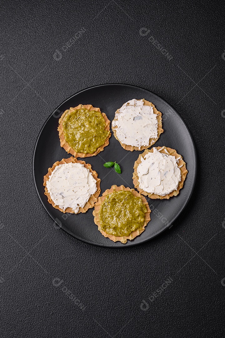 Petiscos redondos com chips crocantes ou biscoitos com cream cheese e pesto num prato de cerâmica