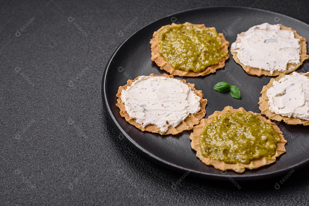 Petiscos redondos com chips crocantes ou biscoitos com cream cheese e pesto num prato de cerâmica