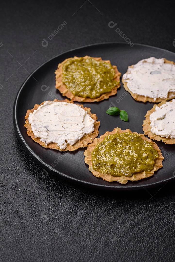 Petiscos redondos com chips crocantes ou biscoitos com cream cheese e pesto num prato de cerâmica