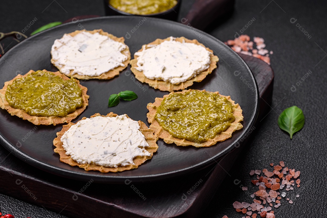 Petiscos redondos com chips crocantes ou biscoitos com cream cheese e pesto num prato de cerâmica